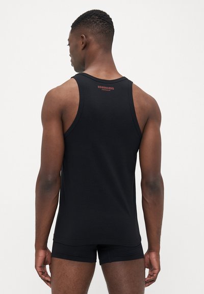 Mann von hinten gesehen, der ein schwarzes ärmelloses Tanktop und passende schwarze Boxershorts vor einem schlichten weißen Hintergrund trägt.