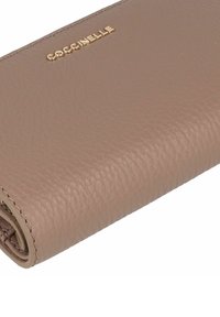 Portafoglio in pelle taupe strutturata, piegato con logo Coccinelle in oro sulla superficie, che mostra una cucitura fine lungo i bordi.