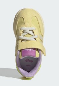 Yellow sneaker with suede and mesh material, elastic laces, and hook-and-loop strap. Purple inner lining and pink branding detail on tongue.