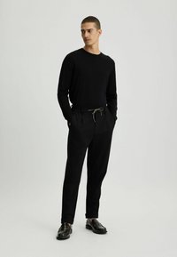 Schwarz langärmliges Shirt, schwarze tapered Hose mit elastischem Bund und grauem Kordelzug sowie schwarzen Lederschuhen. Einfaches Design, glatte Textur.