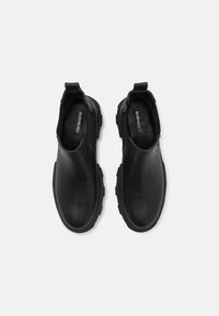 Zapatos de piel negra tipo slip-on con una superficie lisa, punta redondeada y suela de goma texturizada. Incluyen tiradores para facilitar el uso.