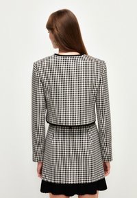 Mustap-white ruudullinen bleiseri, jossa on lyhennetty malli, pitkät hihat ja mustat reunat. Asusteeseen kuuluu pleated-musta hame, jossa on taskut.