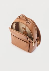 Light brown leather backpack with gold zippers, one main compartment partially open showing beige interior lining with logo pattern.