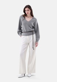 Grau gestrickter Pullover mit V-Ausschnitt und Ballonärmeln, kombiniert mit hochtaillierten, weißen weiten Hosen und weißen spitzen Absätzen.