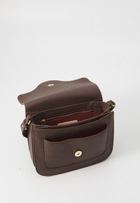 Brown leather shoulder bag with a textured finish, rounded flap top, gold hardware, and two compartments, including a zipper pocket.