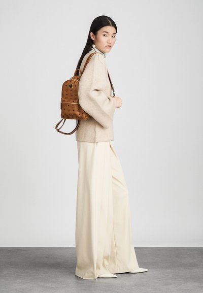 Brun mönstrad ryggsäck med justerbara remmar, texturerad yta och dragkedja. Bärs med en överdimensionerad beige tröja och vida krämfärgade byxor.
