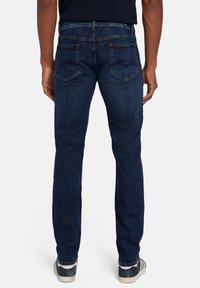 Jean en denim bleu foncé avec une coupe droite, dotés de deux poches arrière et de coutures orange. Le pantalon a une texture lisse et un design classique.