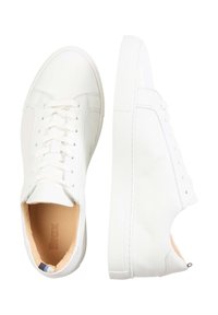 Sneakers bianchi in pelle dalla superficie liscia, suole in gomma piatte e sistema di allacciatura tradizionale. Presentano una fodera interna beige e un branding minimale.