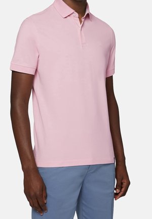 Lyserød polo med krave, korte ærmer og et diskret logo på brystet. Fremstillet af blødt, åndbart stof. Parret med blå bukser.