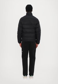 Black puffer jacket with horizontal quilting, high collar, and a cropped design, paired with black pants and light-colored shoes.