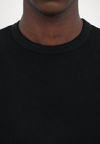 Čierny rebrovaný pletený sveter s klasickým okrúhlym výstrihom. Textúra je hladká a látka sa zdá byť mäkká a elastická.