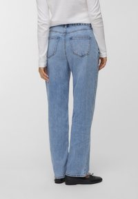 Světlomodré džíny s uvolněným střihem, s dvěma zadními kapsami a klasickým pětikapsovým designem, nošené s černými plochými botami.