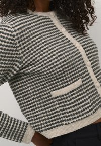 Cardigan lavorato a maglia in grigio e crema, con un motivo testurizzato, colletto rotondo, chiusura con bottoni e una tasca a sinistra.