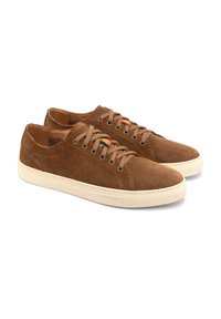 Baskets basses en suede marron avec des semelles en caoutchouc crème, présentant des œillets en métal et des accents en tissu coloré sur le côté près des lacets.