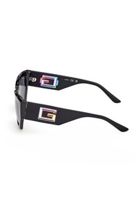 Lunettes de soleil noires avec des branches épaisses rectangulaires ornées de logos "G" irisés de chaque côté et des verres teintés foncés.