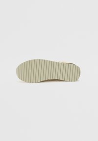 Bunden af en sko med en struktureret, lys beige gummisål, der har lodrette riller for bedre greb og en glat finish ved hælen.