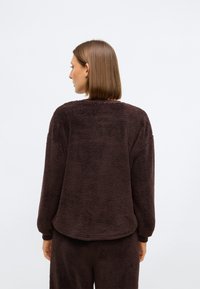 Brūns fliša pulovers ar strukturētu virsmu, apaļu kaklu un nokrītošām plecu šuvēm, ar brīvu piegriezumu un ribotiem piedurknēm.