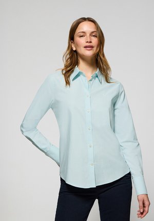 Camicia azzurro chiaro con bottoni, maniche lunghe, colletto classico e orlo curvo. Realizzata in un tessuto morbido con una leggera lucentezza.