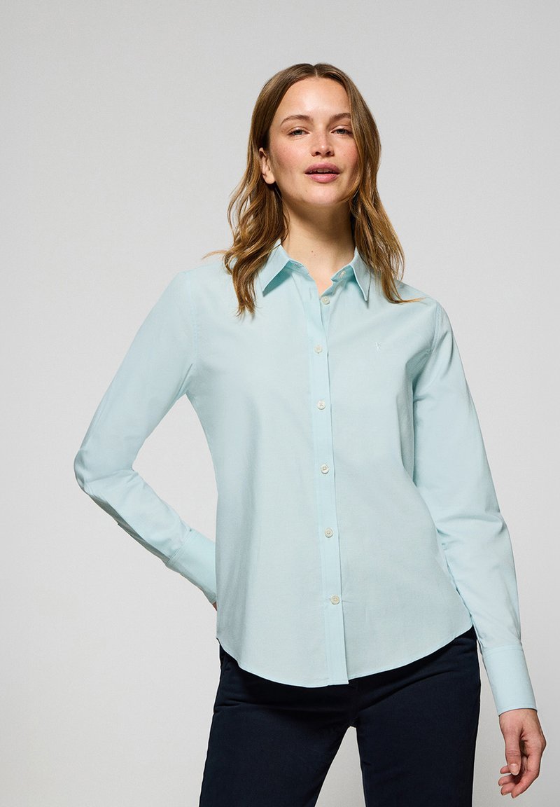 Jasnoniebieska koszula z długimi rękawami, klasycznym kołnierzykiem i zaokrąglonym dołem. Wykonana z gładkiego materiału o delikatnym połysku.