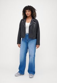 Black faux leather biker jacket with zip closure, white tank top, and light blue wide-leg jeans. Silver sneakers complete the outfit.