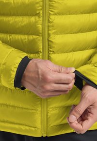 Mani che aggiustano l'orlo interno nero di una giacca trapuntata gialla brillante con zip frontale.