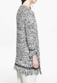 Długi czarnobiały sweter dziany o teksturowanym wykończeniu, z frędzlami na rękawach i u dołu, zaprojektowany w luźnym fasonie.