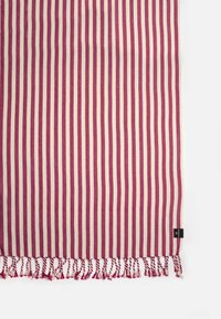 Gestreepte katoenen deken in maroon en crème, met franjes aan één rand en een klein decoratief label aan de zijkant.