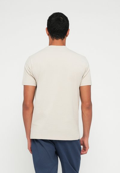 T-shirt beige à manches courtes, col rond, confectionné en tissu doux, présentant un dos uni avec des détails de couture minimalistes.