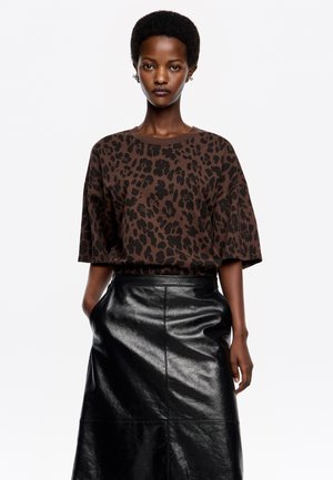 Camiseta marrón de manga corta con estampado de leopardo negro; combinada con una falda de cuero negro brillante, de cintura alta y con detalles de bolsillo.