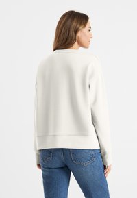 Lichtgrijze sweatshirt met een ontspannen pasvorm, ribgebreide manchetten en een ronde halslijn. Gemaakt van zachte stof met een gladde textuur.