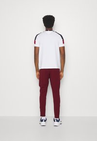 Vit kortärmad t-shirt med marinblå och burgundyröda axeldetaljer, kombinerad med burgundyröda slim-fit byxor och vita sneakers med marinblå detaljer.