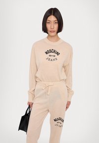 Bežna loungewear komplet, ki vključuje dolgosleeven top z črnim napisom in ujemajoče se hlače s pasom na vrvico. Dvobarvna pletena tekstura.