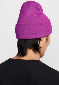 Berretto di maglia viola con risvolto, caratterizzato da una texture a coste. Indossato con una maglietta nera, mostrando la vista posteriore del berretto e dei capelli.