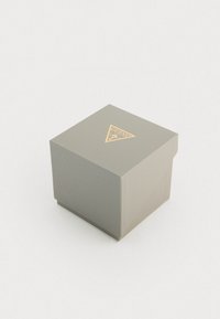 Scatola rettangolare grigia con superficie texturizzata, dotata di un logo triangolare dorato sulla parte superiore. Design semplice e geometrico.