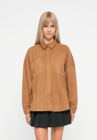Brown faux suede shirt jacket with a collar, two chest pockets, and a relaxed fit, featuring gray button accents and long sleeves.