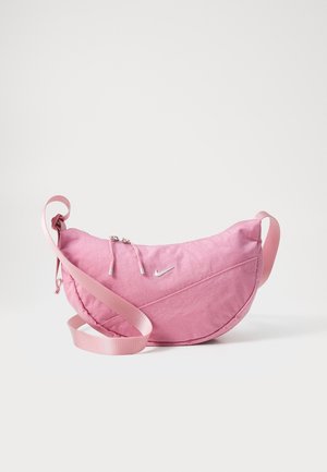 Pink crescent-shaped Nike shoulder bag with adjustable strap and zippered main compartment on white background.