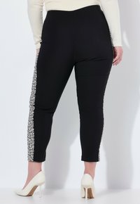 Czarne legginsy o dopasowanym kroju, z bocznym panelem w leopardzi wzór. Gładka tekstura, długość do kostek, w połączeniu z białymi szpilkami.