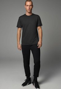 Zwart sport t-shirt met korte mouwen, gecombineerd met zwarte slim-fit joggers en zwarte sneakers, tegen een effen achtergrond.