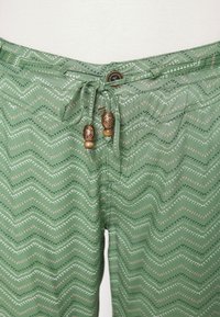 Green shorts with a zigzag pattern in white, pink, and dark green, featuring a drawstring with decorative wooden beads and a button closure.