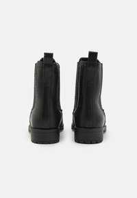 Botas negras de cuero hasta el tobillo con un acabado texturizado, paneles laterales elásticos y una suela de goma resistente. Cuenta con costuras decorativas.