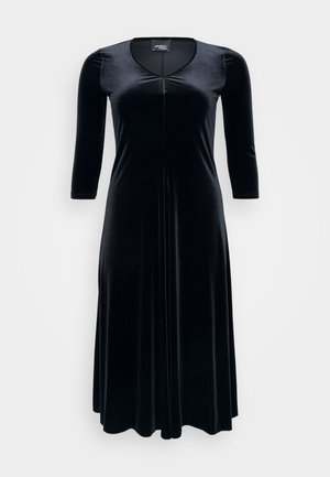 Sorte fløyelskjole med V-hals, 3/4 ermer og en flytende skørt. Har en front søm detalj og glatt, teksturert stoff.