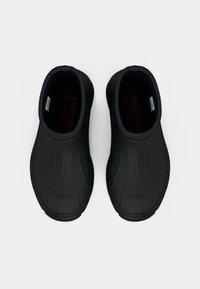 Chaussures noires en caoutchouc à enfiler avec une texture lisse, un design incurvé et une semelle extérieure rainurée ; dotées d'une doublure à motif rouge.