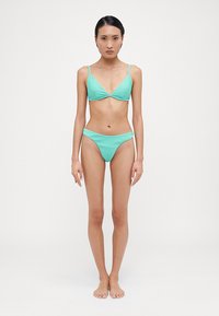 Turkis ribbet bikinitopp med trekantet topp og lavtailte truser. Materialet er glatt med tynne stropper og design med minimal dekning.