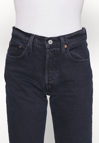 Jeans de mezclilla de color azul oscuro con corte recto, que cuentan con un cierre de botón plateado y dos bolsillos delanteros. Textura sutil con acentos de costura naranja.