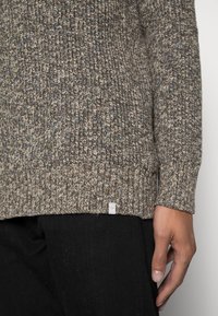 Maglione lavorato a maglia marrone con tessuto testurizzato e macchie blu, polsini e orlo a coste, e piccolo etichetta del marchio in basso.