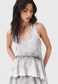 Top sin mangas casual en un gris claro y desgastado con bordes deshilachados. Diseño de peplum acampanado con escote redondo y sin herrajes visibles.