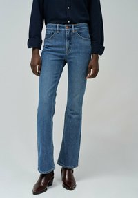 Modré zvonové džíny vyroben�é z denimu s středně vysokým pasem, designem s pěti kapsami a jemným detailem šití, ve spojení s tmavě hnědými botami na podpatku.