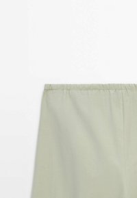 Tissu vert clair avec ceinture élastique cousue, présenté à plat sur fond blanc.
