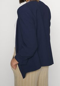 Navy blue blazer with a loose fit, textured fabric, and rolled sleeves, paired with beige high-waisted striped trousers.