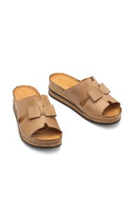 Brązowe skórzane klapki z odkrytymi palcami i detalem w postaci kokardki. Korek jako podeszwa z akcentami w postaci stębnowania. Gładka tekstura, swobodny styl i łatwe zakładanie.